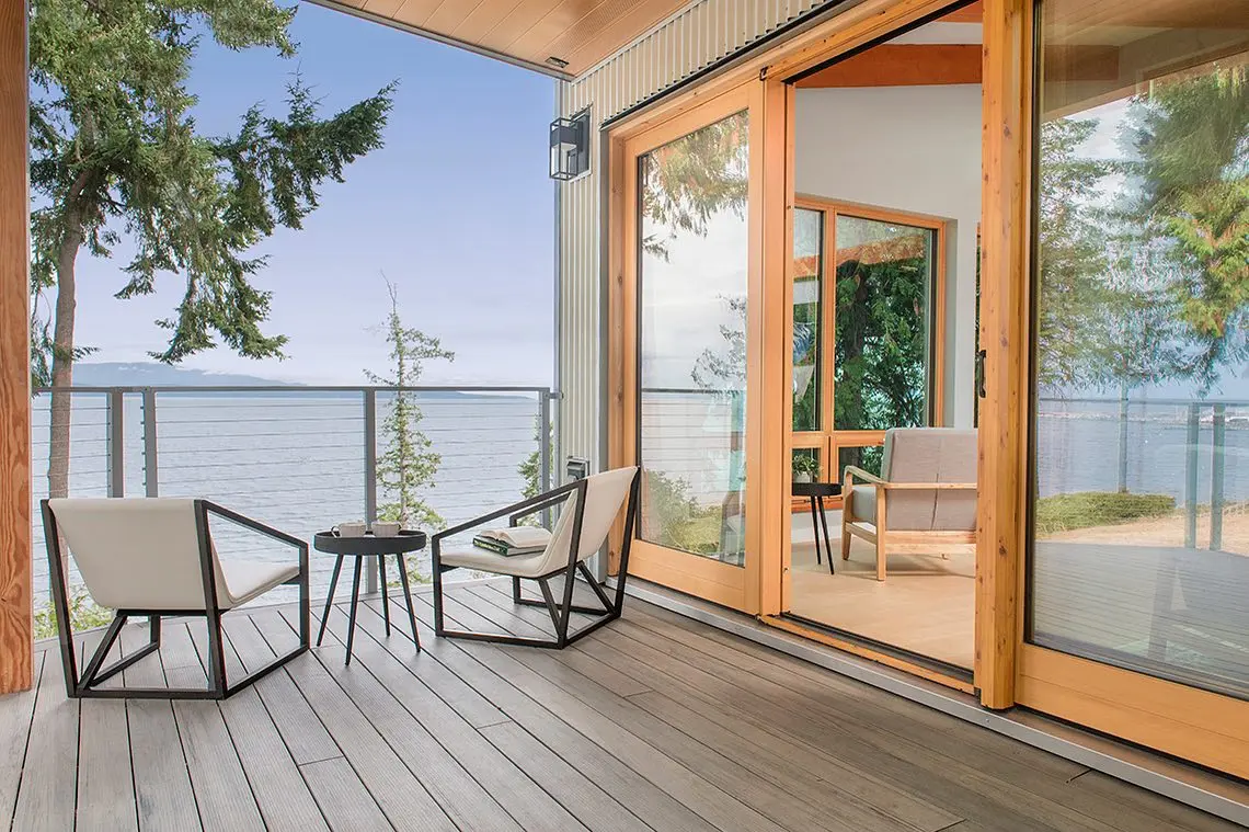 Open Fenstür wood lift-and-slide door connecting a bright home to an oceanfront terrace